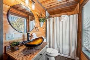 This full bathroom offers modern comfort with fresh towels, toilet paper, hand soap, body soap, and a hair dryer. Featuring a walk-in shower, granite vanity, and cozy cabin charm, it's stocked with essentials to ensure a refreshing & hassle-free stay