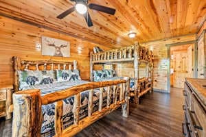 Cozy rustic bedroom featuring a handcrafted queen log bed and a queen-over-queen bunk. Enjoy direct access to the deck, a spacious dresser, and a private full bathroom. Perfect for families or groups looking for comfort and cabin charm!