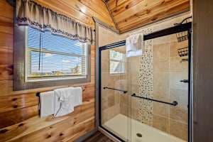 This full bathroom offers modern comfort with fresh towels, toilet paper, hand soap, body soap, and a hair dryer. Featuring a walk-in shower, granite vanity, and cozy cabin charm, it's stocked with essentials to ensure a refreshing & hassle-free stay